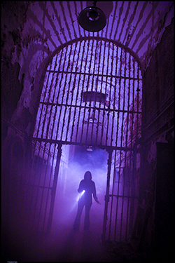 silhouette of a person holding a flashlight in a dark, foggy cellblock