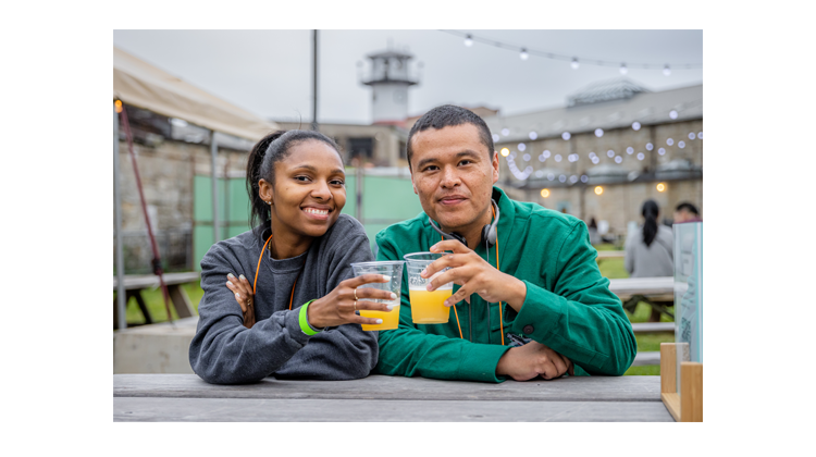 Two people holding pints of beer and smiling while sitting at a picnic table