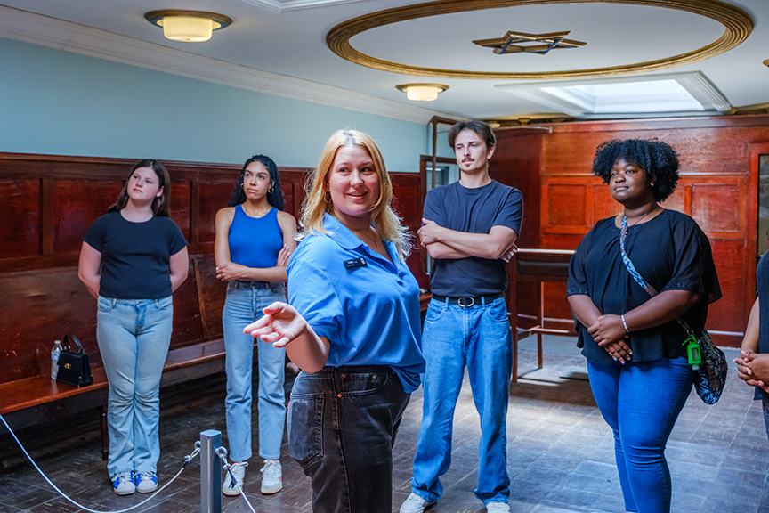 A tour guide at Eastern State showing visitors the Synagogue. She is gesturing towards something off screen where the visitors are looking.